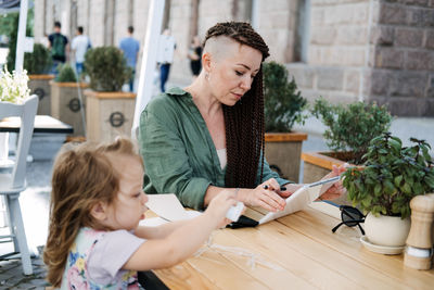 Busy successful mother and business owner with cell phone and tablet having breakfast with her