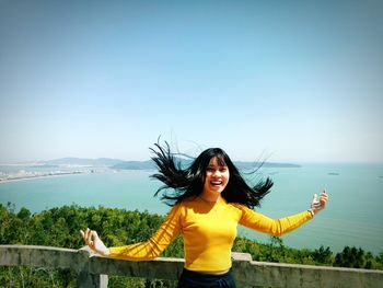 Portrait of smiling young woman standing on mountain against clear sky