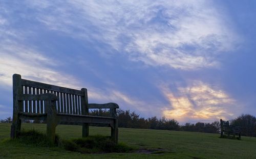 Empty bench on field against sky during sunset