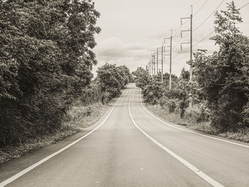 Empty road amidst trees against sky