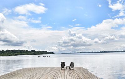 Deck chairs on jetty over lake against sky