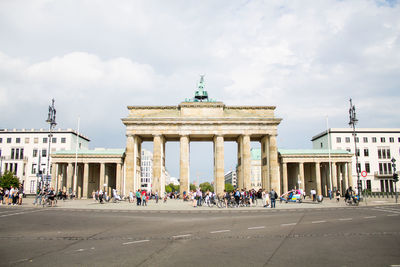 People in front of historical building against cloudy sky