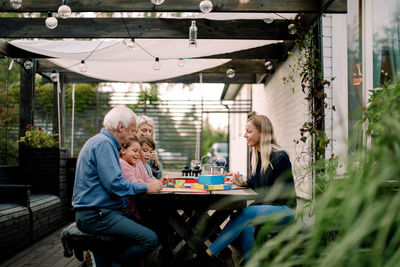 Smiling family playing board game while sitting at table in patio