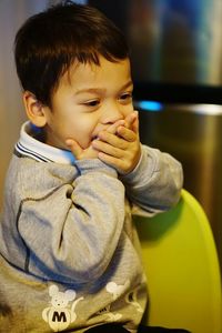 Close-up of boy covering mouth while sitting on chair