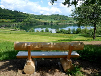 Empty bench on field by trees against sky