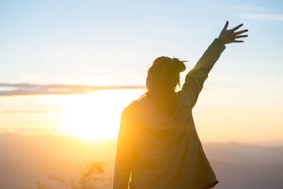 Rear view of woman standing against sky during sunset