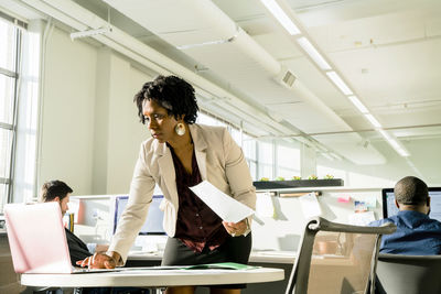 Businesswoman using laptop computer while businessmen working in background