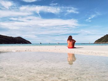 Rear view of woman standing on beach against sky