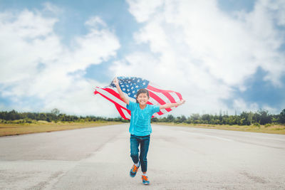 Portrait of smiling teenage girl with american flag standing on road