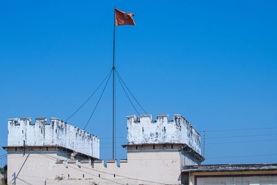 Low angle view of flag against building against clear blue sky