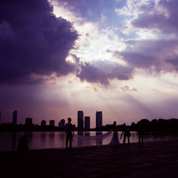 Silhouette people standing by sea against sky during sunset