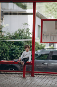 Full length portrait of boy sitting on bus stop 