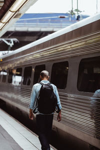 Rear view of man carrying backpack while walking by train on railroad station platform