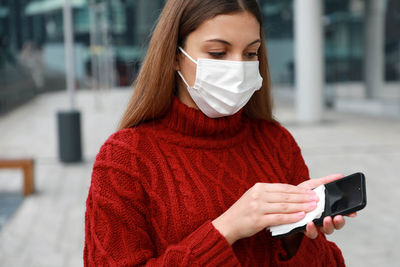 Young woman wearing man cleaning mobile phone outdoors