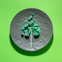 Creative sweet christmas tree made of pieces of fractured green lollipop on grey plate on green.