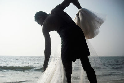 Fisherman holding net while standing at beach against sky