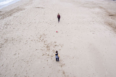 High angle view of woman playing soccer with son on sand at beach