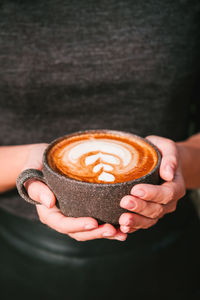 Woman in a black clothing holds coffee in a grey ceramic cup, vertical photo.