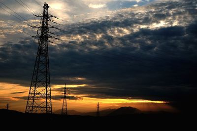 Low angle view of electricity pylon against cloudy sky