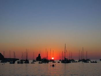 Sailboats moored in sea at sunset