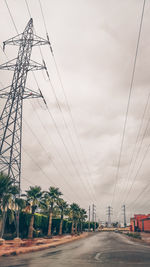 Road by electricity pylon against sky in city