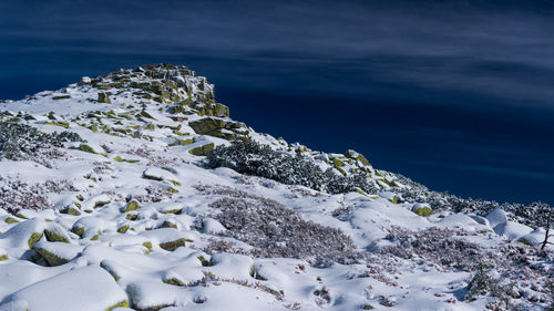 Snow covered rocks in sea against sky