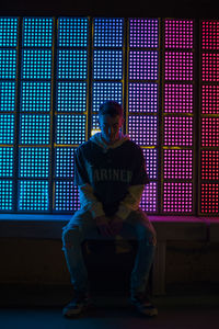 Full length of young man sitting against illuminated window