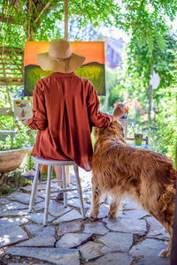 Artist working on her art canvas painting outdoors with golden retriever keeping her company. 