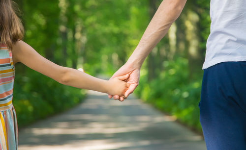 Midsection of daughter and father holding hands while standing outdoors