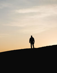 Silhouette of woman standing on landscape at sunset