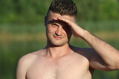 Close-up portrait of shirtless young man shielding eyes