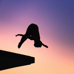 Low angle view of silhouette mid adult woman jumping against clear sky during sunset