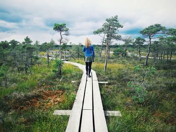 Rear view of woman standing on footbridge against sky