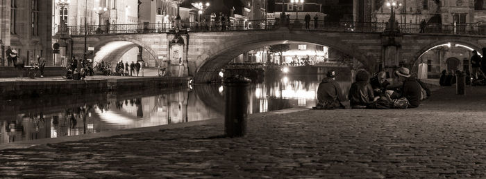 People sitting on illuminated bridge in city