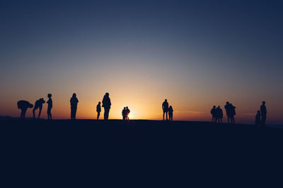 Silhouette people at beach against clear sky during sunset