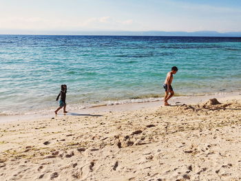 Siblings walking at beach against sky