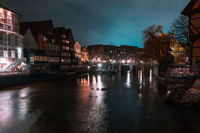 Illuminated buildings by river against sky at night