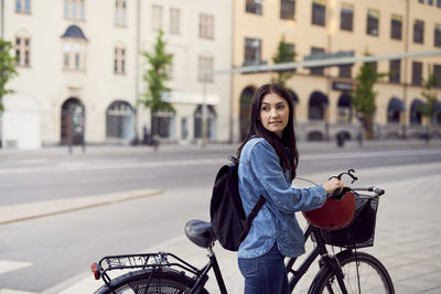 Mid adult woman looking away while walking with bicycle in city