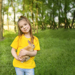 The girl holds a real rabbit against the background of green plants in the sun. 