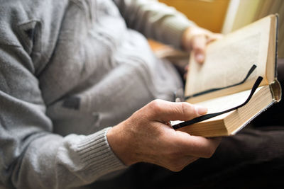 Midsection of man holding book and eyeglasses at home