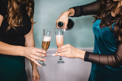 Tilt shift image of friends holding drinking glasses while standing against wall at home