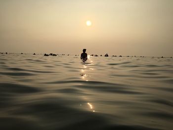 Silhouette person in water at beach against sky during sunset