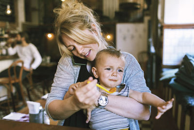 Mid adult mother trying to feed baby boy in restaurant