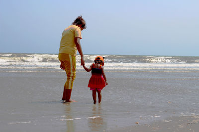 Rear view of mother and daughter standing at beach against clear sky