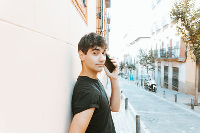 Young woman looking away while standing against wall