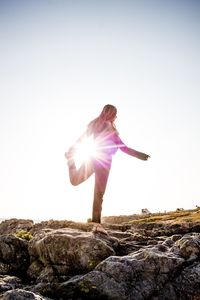 Woman standing on rock against sky during sunny day