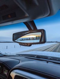 Close-up of rearview mirror and car windshield on snowy road in the winter with sunset