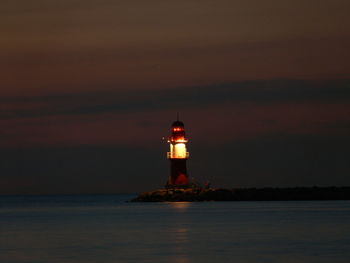 Lighthouse by sea against sky at night