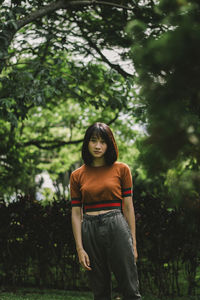 Portrait of young woman standing against trees in park