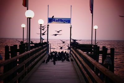 People on jetty by pier against sky during sunset